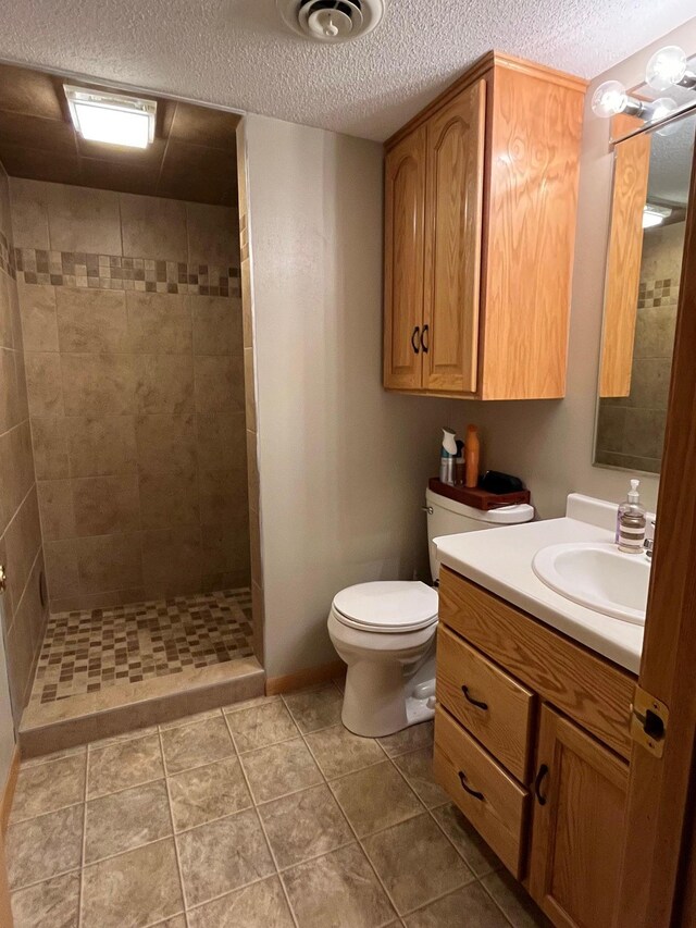 bathroom featuring tile patterned floors, toilet, a textured ceiling, a tile shower, and vanity