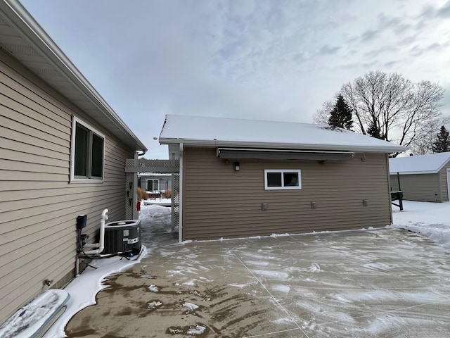 snow covered back of property featuring an outbuilding, central AC unit, and a pergola