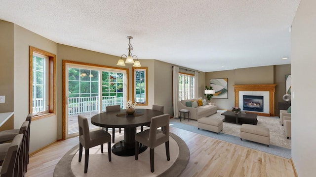 dining space with a textured ceiling, a notable chandelier, a fireplace, and light hardwood / wood-style flooring