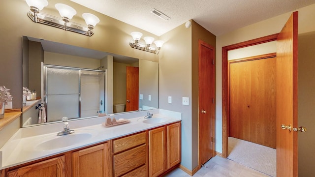 bathroom featuring vanity, toilet, a shower with shower door, and a textured ceiling