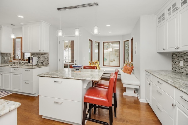 kitchen featuring sink, decorative light fixtures, a center island, light wood-type flooring, and white cabinets