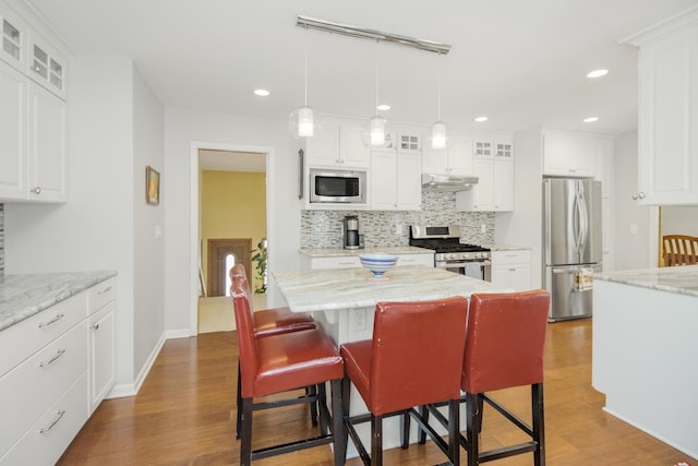 kitchen featuring light stone countertops, stainless steel appliances, a center island, and white cabinets