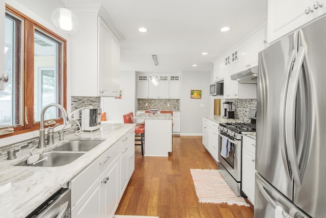 kitchen with sink, appliances with stainless steel finishes, pendant lighting, light stone countertops, and white cabinets