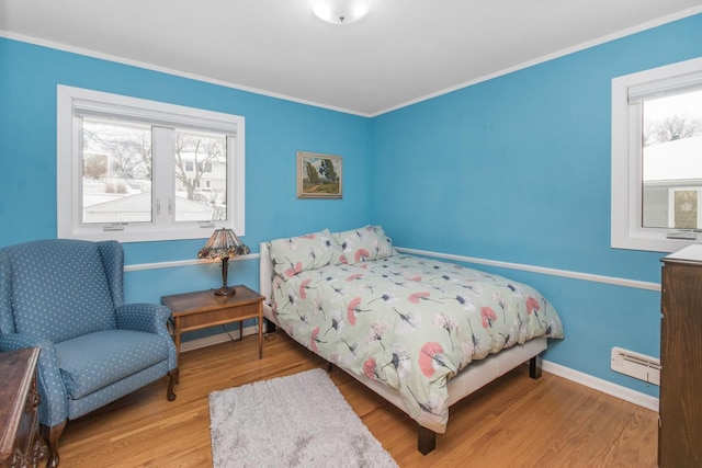 bedroom with ornamental molding, a baseboard heating unit, and light hardwood / wood-style floors