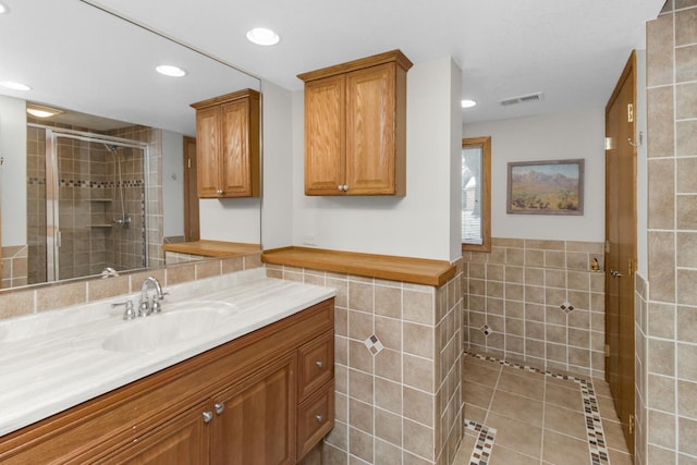 bathroom featuring walk in shower, vanity, tile patterned flooring, and tile walls