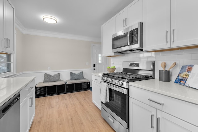 kitchen featuring white cabinets, decorative backsplash, light hardwood / wood-style floors, stainless steel appliances, and crown molding