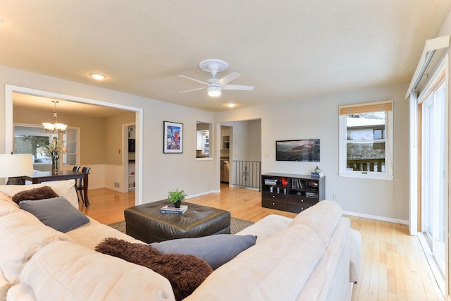 living room featuring ceiling fan with notable chandelier, a textured ceiling, and light wood-type flooring