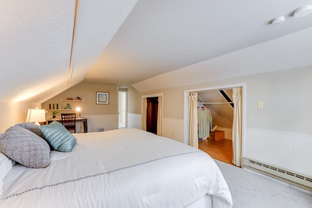 bedroom featuring lofted ceiling, a spacious closet, a textured ceiling, a baseboard radiator, and a closet