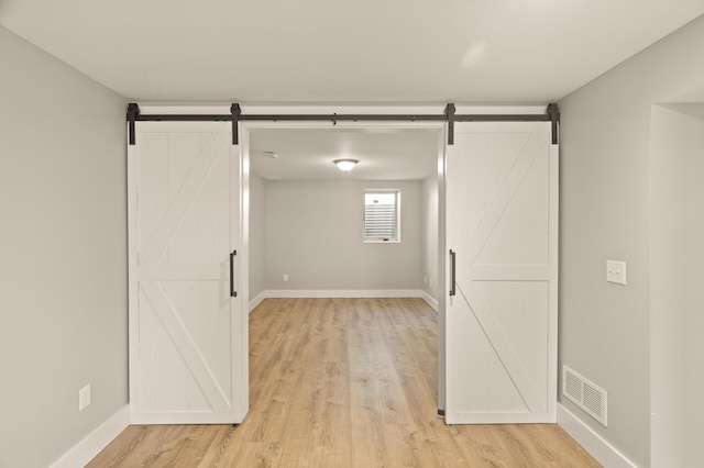 empty room with a barn door, visible vents, light wood-style flooring, and baseboards