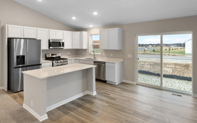 kitchen with lofted ceiling, sink, appliances with stainless steel finishes, white cabinetry, and a center island