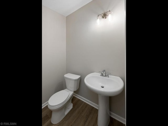 half bathroom featuring a sink, wood finished floors, toilet, and baseboards