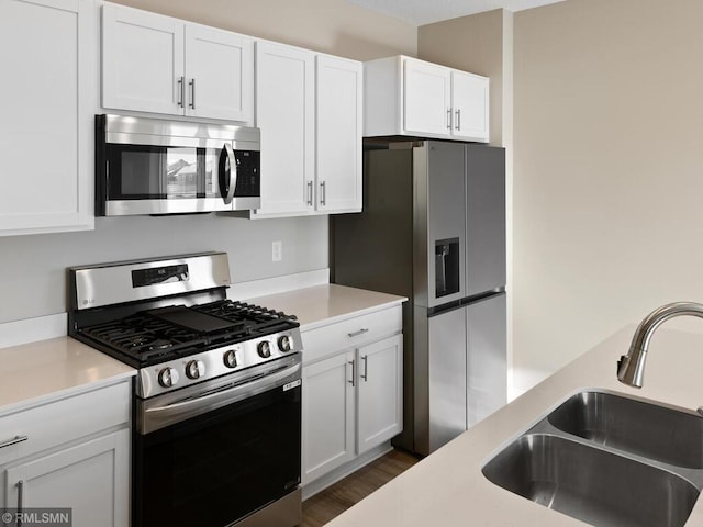 kitchen with stainless steel appliances, a sink, white cabinets, light countertops, and dark wood-style floors