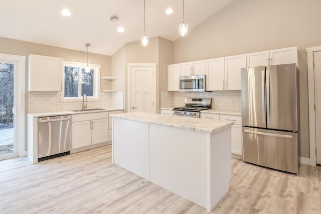 kitchen with white cabinets, appliances with stainless steel finishes, a center island, hanging light fixtures, and a sink