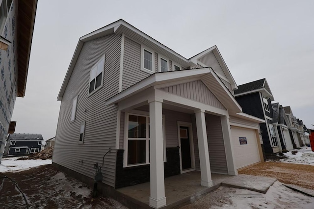 snow covered property with a porch and a garage