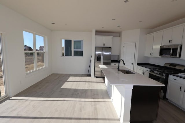 kitchen with white cabinetry, sink, stainless steel appliances, and an island with sink