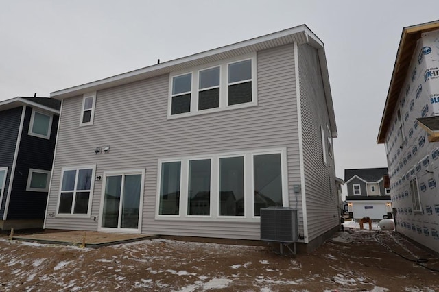 snow covered rear of property featuring central AC and a patio