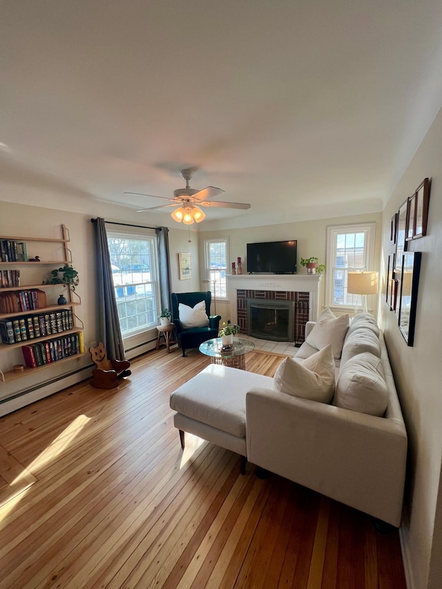 living room with light hardwood / wood-style floors, a tile fireplace, ceiling fan, and baseboard heating