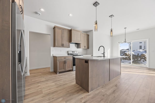 kitchen with sink, hanging light fixtures, an island with sink, stainless steel appliances, and light hardwood / wood-style floors