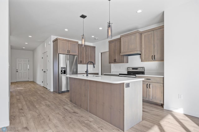 kitchen with sink, hanging light fixtures, stainless steel appliances, an island with sink, and light wood-type flooring