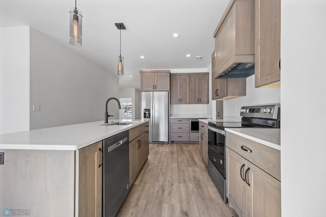 kitchen with appliances with stainless steel finishes, pendant lighting, sink, light hardwood / wood-style floors, and a center island with sink