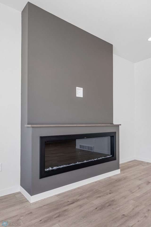 details with a glass covered fireplace, wood finished floors, visible vents, and baseboards