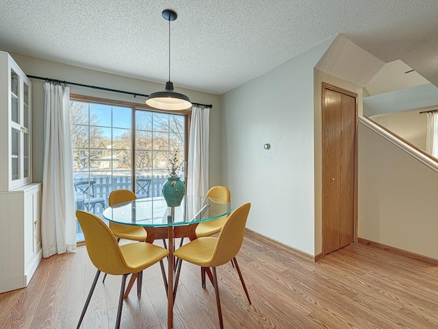 dining area featuring light wood-type flooring, baseboards, and a textured ceiling