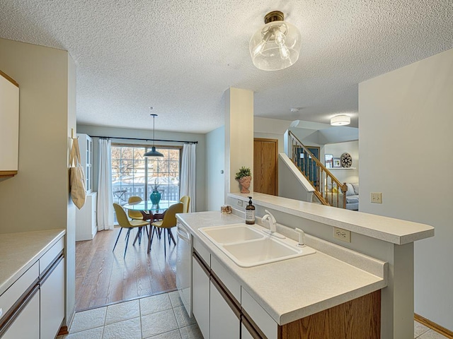 kitchen featuring light countertops, hanging light fixtures, white cabinetry, a sink, and an island with sink