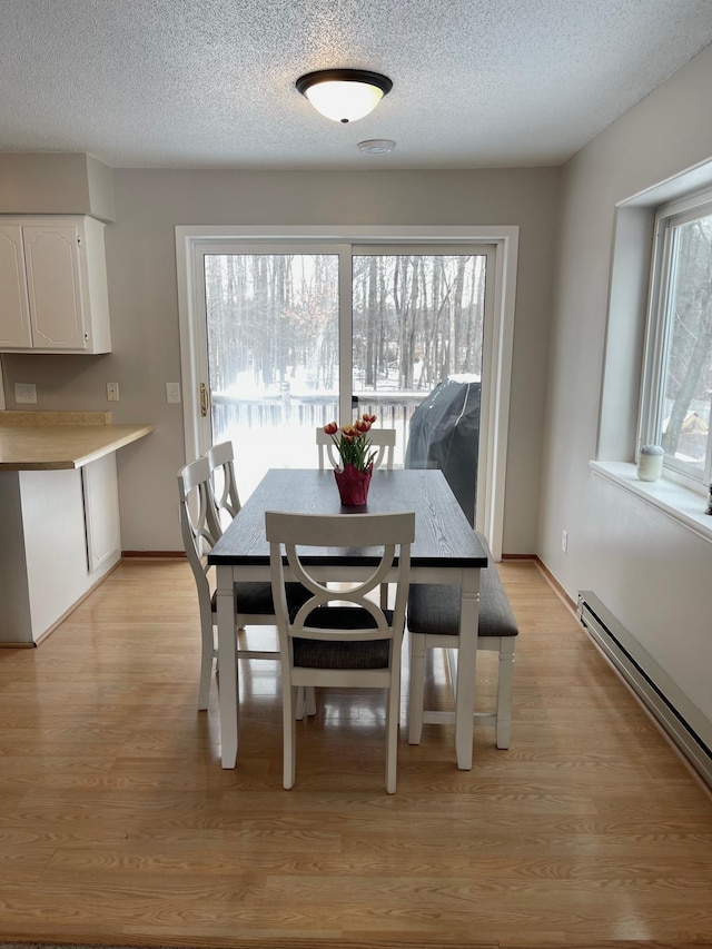 dining area featuring a baseboard radiator, a healthy amount of sunlight, light hardwood / wood-style flooring, and a textured ceiling