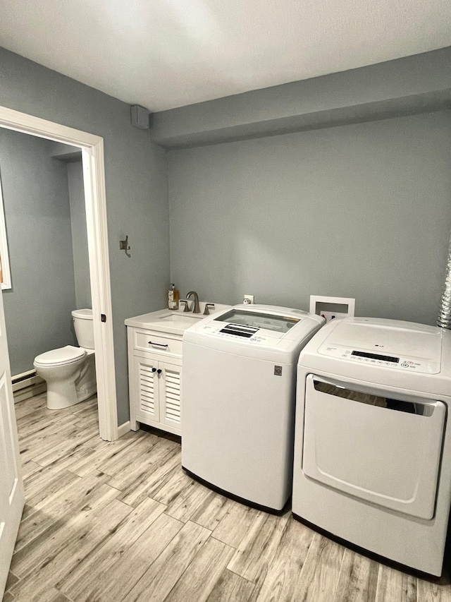 clothes washing area with light hardwood / wood-style flooring, sink, washer and clothes dryer, and baseboard heating