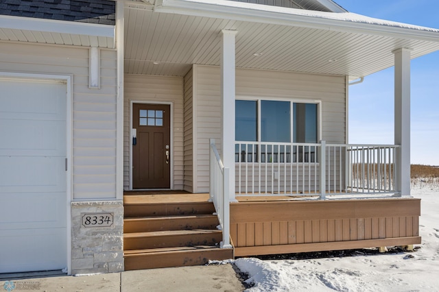 snow covered property entrance featuring a garage and covered porch