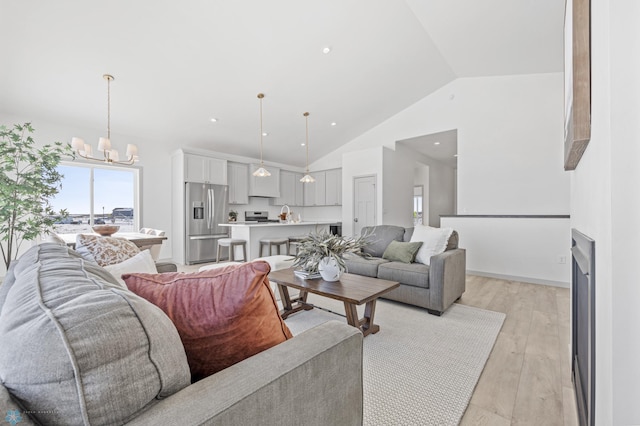 living room featuring an inviting chandelier, a fireplace, high vaulted ceiling, and light wood-type flooring