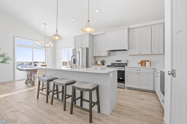 kitchen with a breakfast bar area, decorative light fixtures, a center island with sink, stainless steel appliances, and light hardwood / wood-style floors