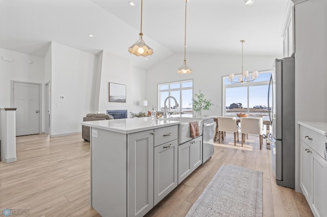 kitchen with sink, light hardwood / wood-style flooring, hanging light fixtures, stainless steel appliances, and a center island with sink