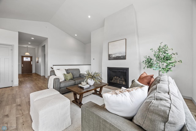 living room featuring a glass covered fireplace, light wood-style floors, baseboards, recessed lighting, and vaulted ceiling