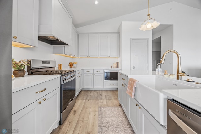 kitchen featuring custom range hood, light countertops, lofted ceiling, stainless steel appliances, and light wood-style flooring
