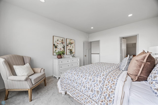 bedroom with recessed lighting, light colored carpet, and a walk in closet