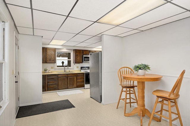 kitchen featuring appliances with stainless steel finishes, a breakfast bar, a paneled ceiling, sink, and dark brown cabinets