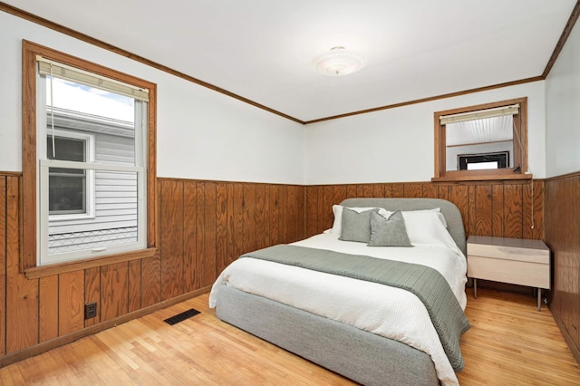 bedroom with crown molding, wooden walls, and light hardwood / wood-style flooring