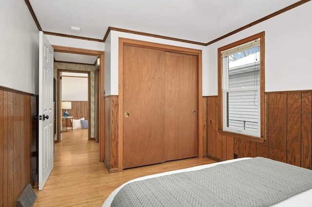 bedroom featuring ornamental molding, a closet, light wood-type flooring, and wood walls