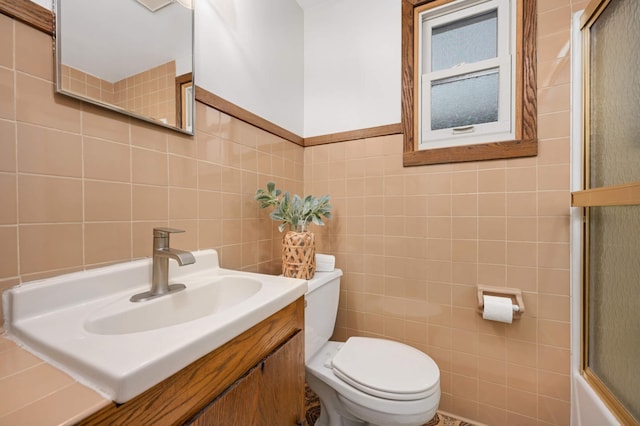 full bathroom with tile walls, vanity, combined bath / shower with glass door, and toilet