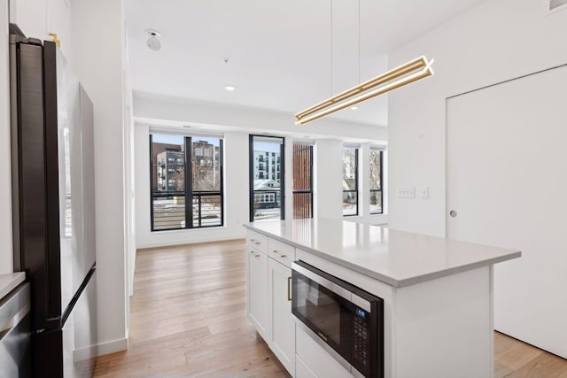 kitchen featuring appliances with stainless steel finishes, white cabinetry, hanging light fixtures, a center island, and light wood-type flooring