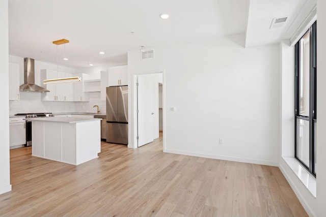 kitchen with appliances with stainless steel finishes, white cabinets, a kitchen island, decorative light fixtures, and wall chimney exhaust hood