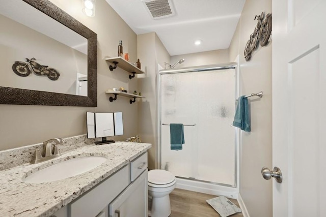 bathroom featuring visible vents, toilet, wood finished floors, vanity, and a shower stall