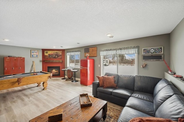 living room featuring billiards, a lit fireplace, a textured ceiling, and wood finished floors