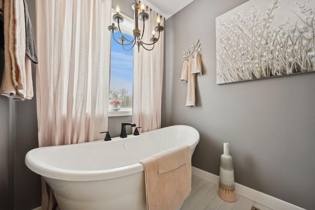 full bath featuring a chandelier, a soaking tub, and baseboards