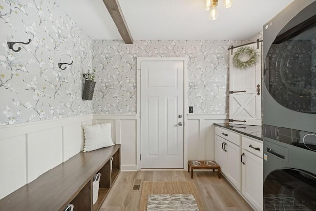 interior space featuring light wood-style floors, stacked washer / dryer, wainscoting, and wallpapered walls