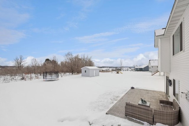 yard layered in snow featuring a trampoline, an outdoor structure, and a shed