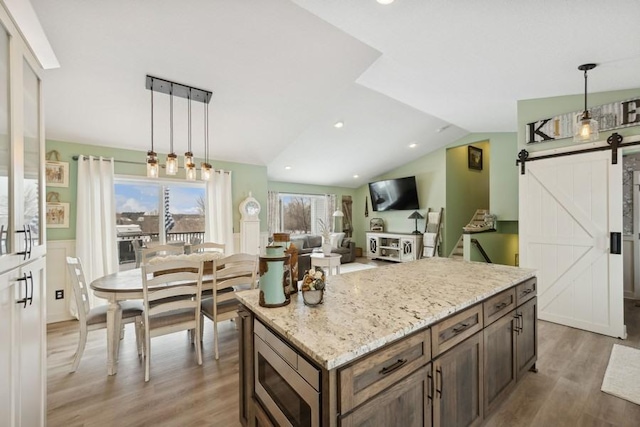 kitchen featuring a barn door, stainless steel microwave, decorative light fixtures, vaulted ceiling, and light wood-type flooring