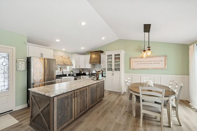 kitchen featuring white cabinets, lofted ceiling, a kitchen island, freestanding refrigerator, and light wood-style floors