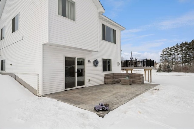 snow covered property with a deck, a patio area, and an outdoor living space